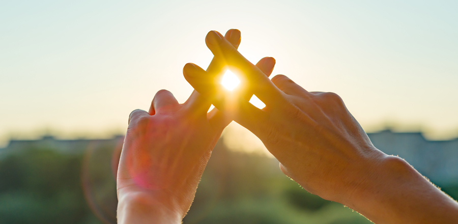 Zwei Hände formen einen Hashtag in Richtung Sonne.