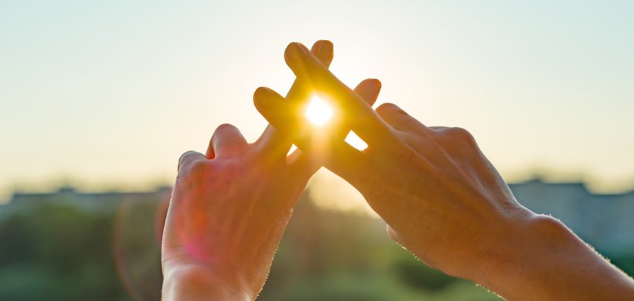 Zwei Hände formen einen Hashtag in Richtung Sonne.
