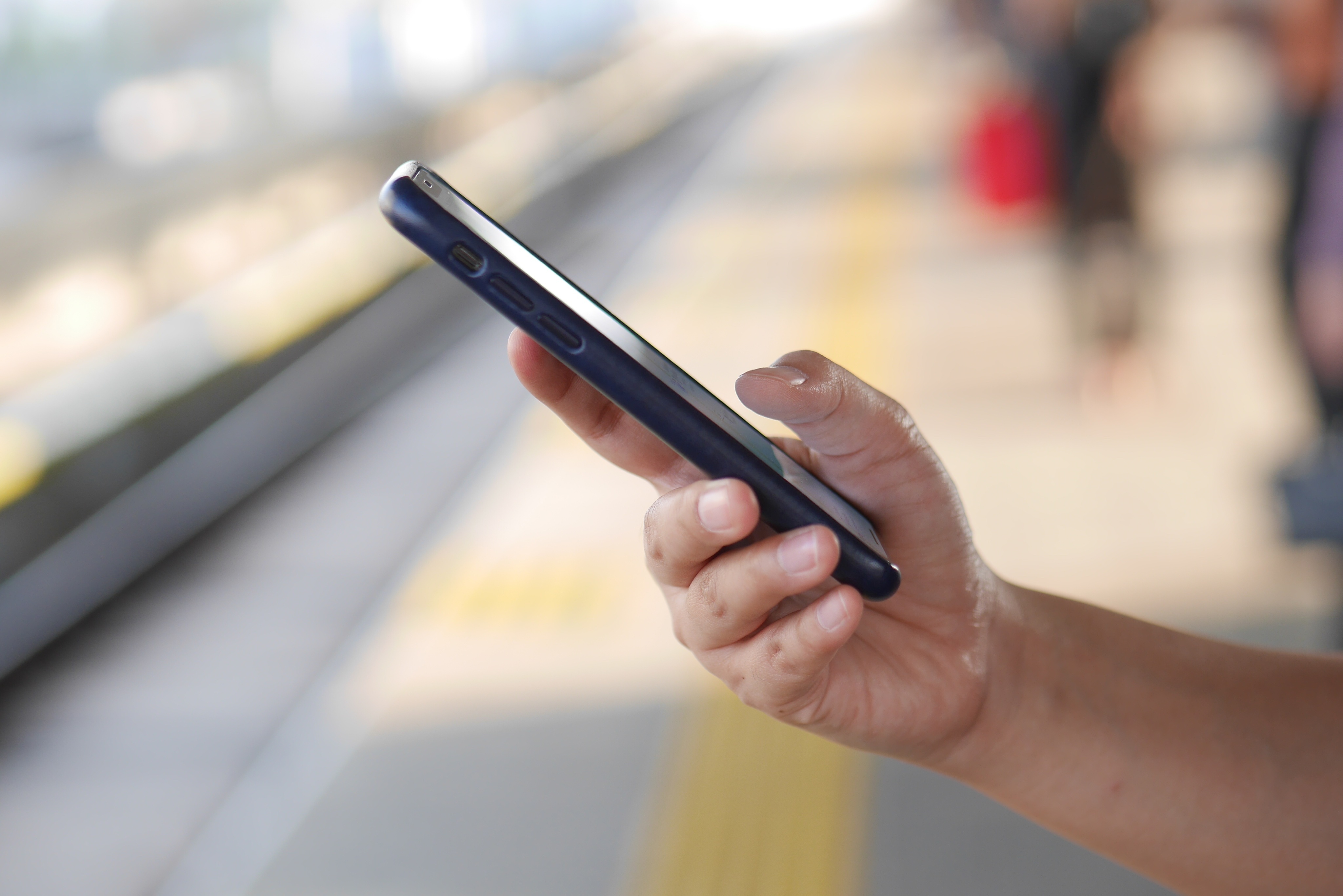 Nahaufnahme eines Mannes der ein Mobiltelefone auf einem Bahnsteig nutzt.