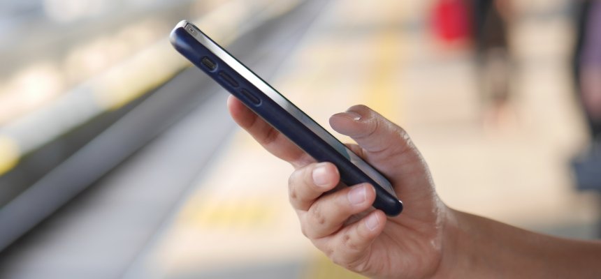 Nahaufnahme eines Mannes der ein Mobiltelefone auf einem Bahnsteig nutzt.