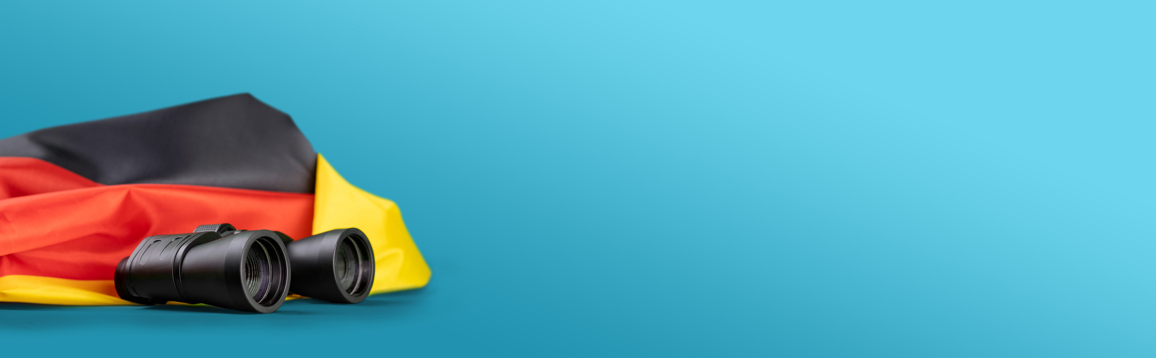 Fernglas und Deutschlandfahne liegen nebeneinander vor blauem Hintergrund.