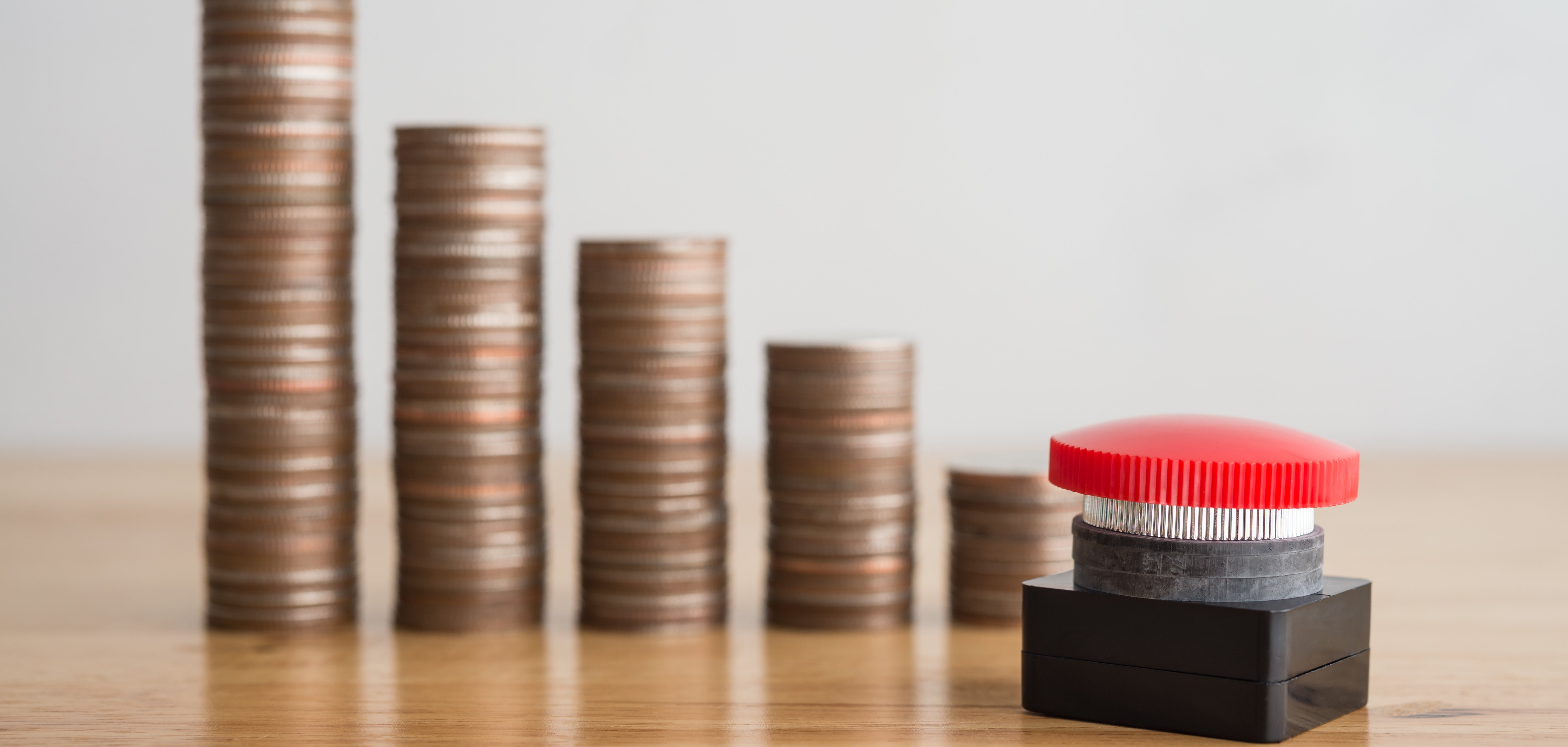 Mehrere Kleingeldstapel aufgereiht, die nach rechts immer kleiner werden. Davor steht ein roter Knopf.