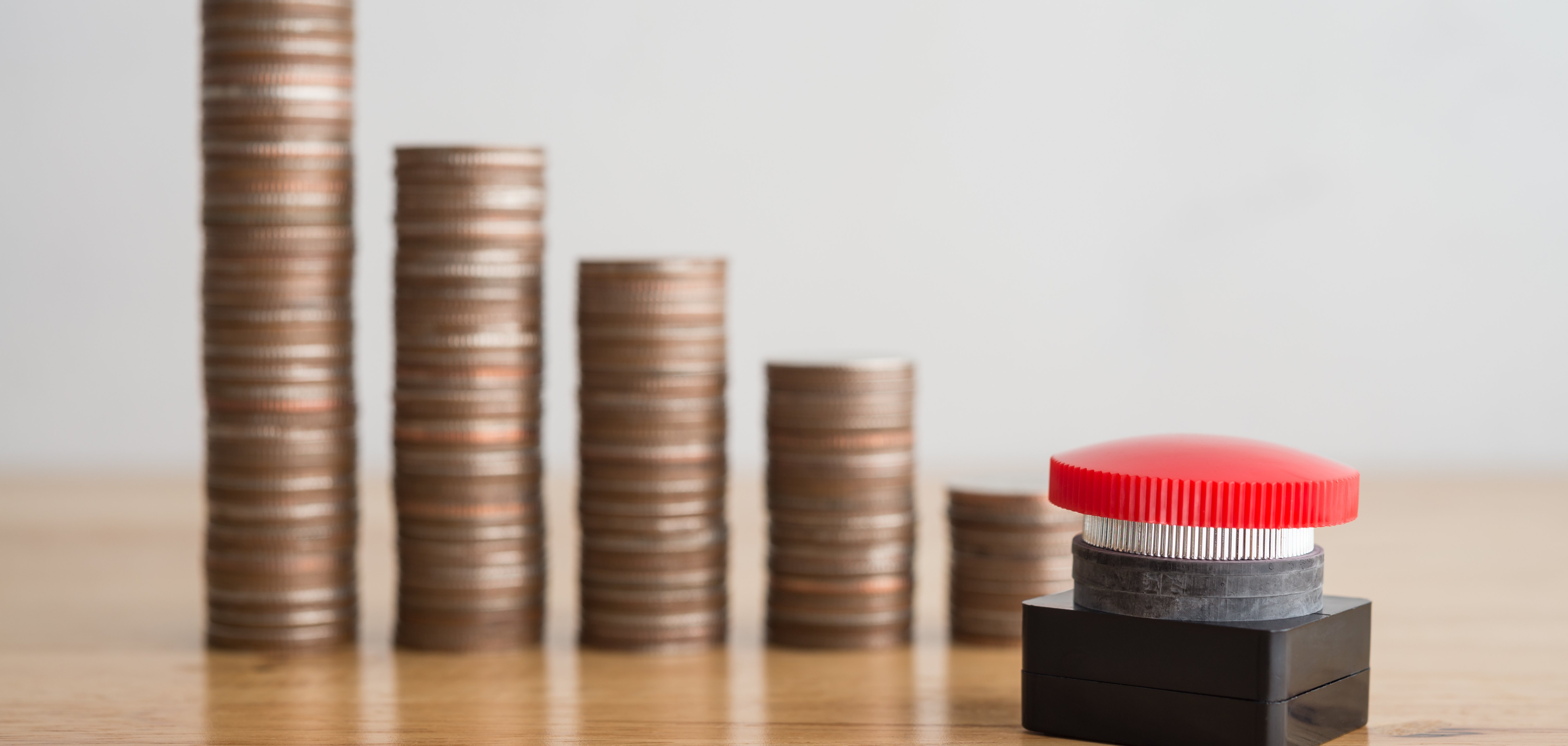 Mehrere Kleingeldstapel aufgereiht, die nach rechts immer kleiner werden. Davor steht ein roter Knopf.