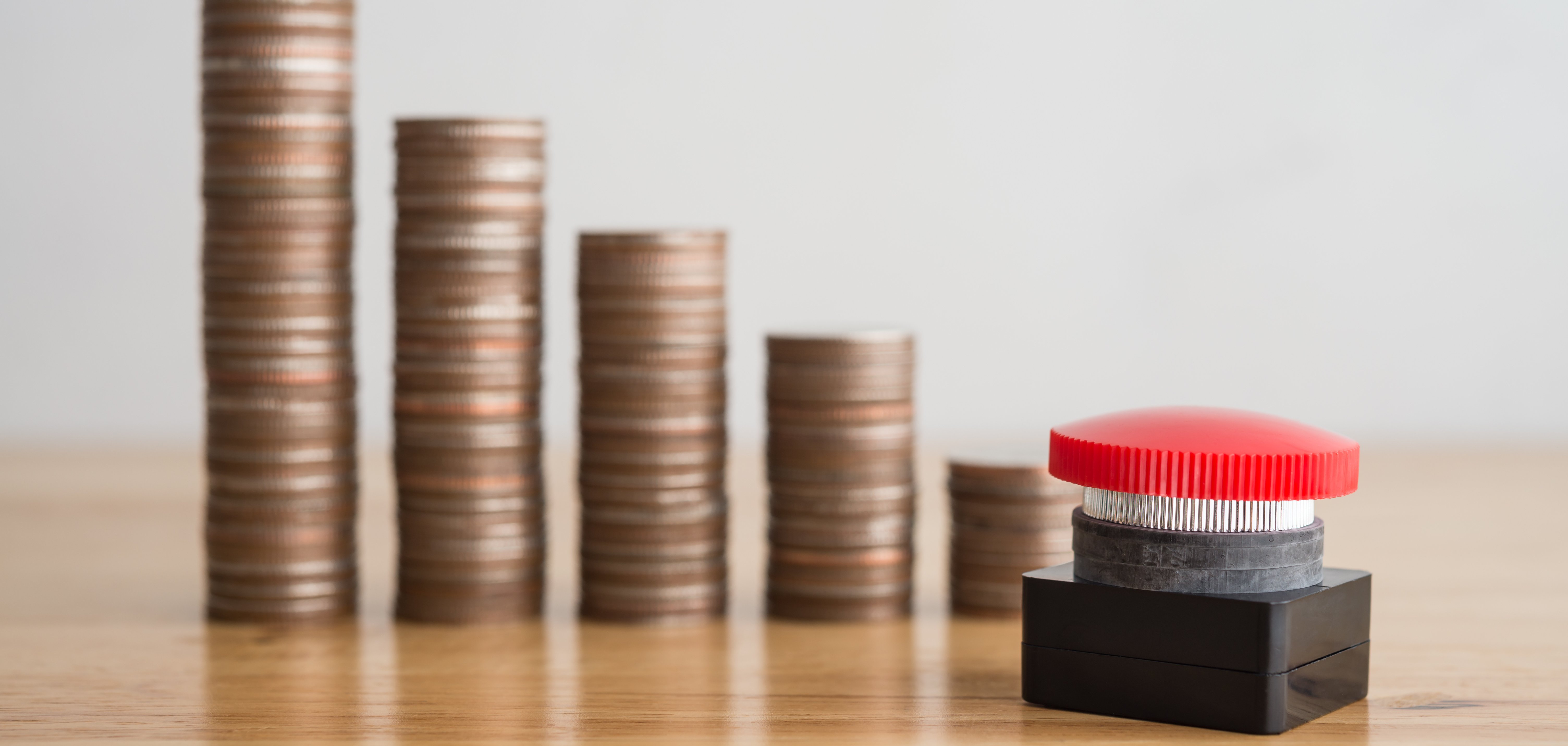 Mehrere Kleingeldstapel aufgereiht, die nach rechts immer kleiner werden. Davor steht ein roter Knopf.