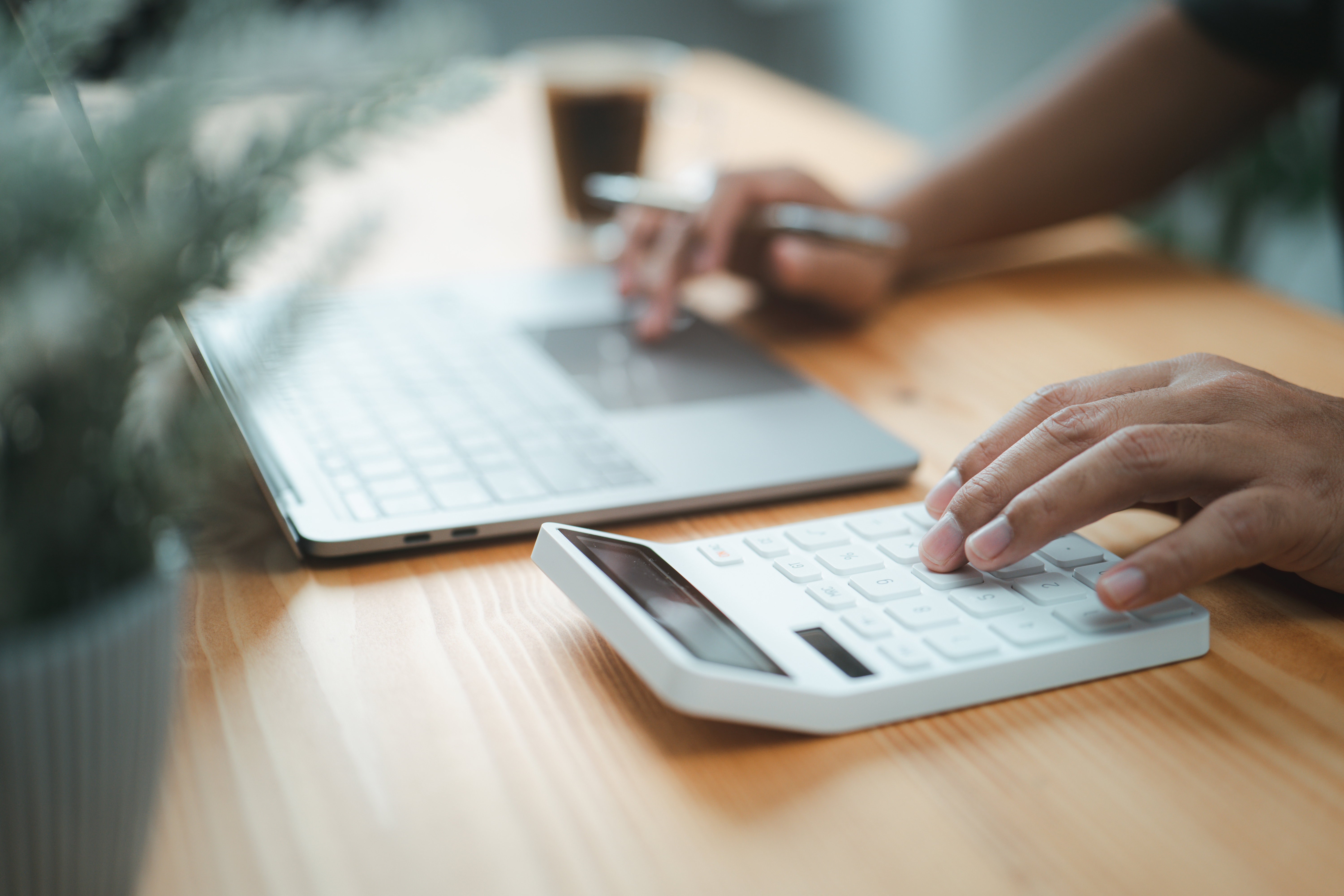 Taschenrechner bedienen Hand eines kaufmännischen Angestellten, der einen Taschenrechner benutzt und etwas in ein Laptop eingibt.