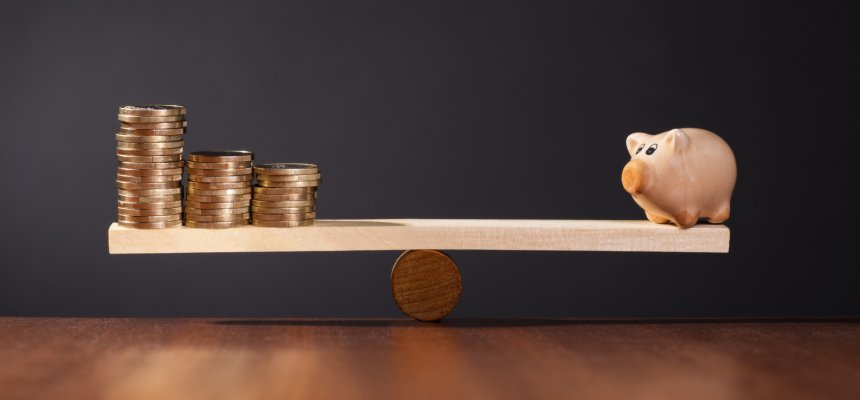 Wippe mit Sparschwein auf der einen Seite und Stapel mit Geld auf der anderen Seite.