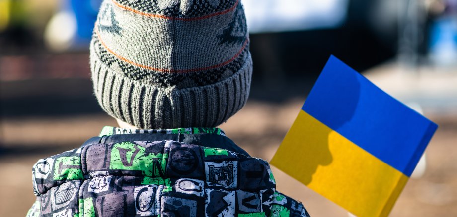 Child or kid with winter clothes, hat and Ukrainian flag, profile of the child is on the flag. War in Ukraine, caused by Putin and Russia