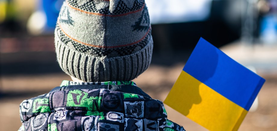 Child or kid with winter clothes, hat and Ukrainian flag, profile of the child is on the flag. War in Ukraine, caused by Putin and Russia