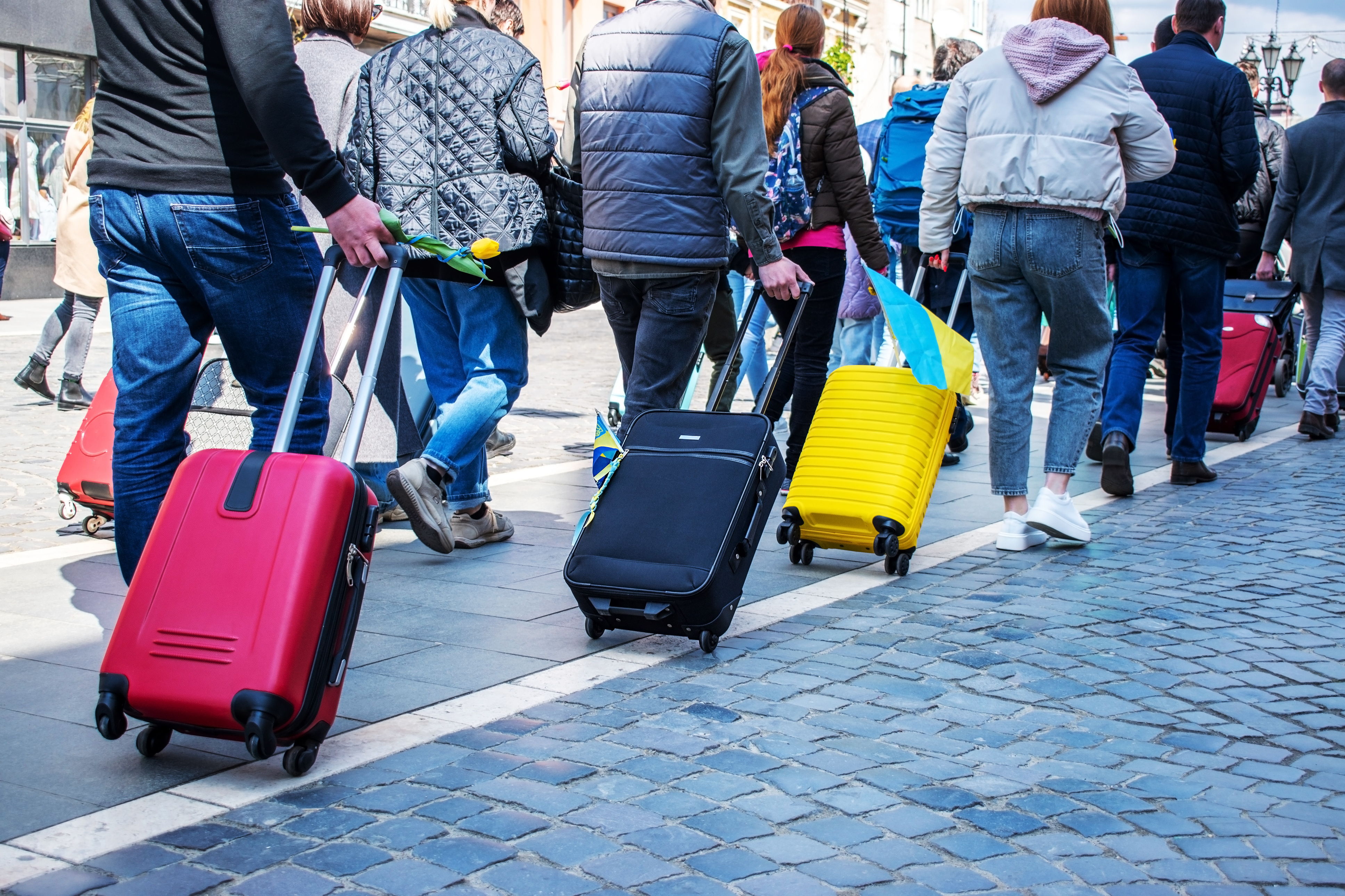 Ukrainische Flüchtlinge verlassen die Ukraine. Menschen mit Rollkoffern gehen hintereinander her.