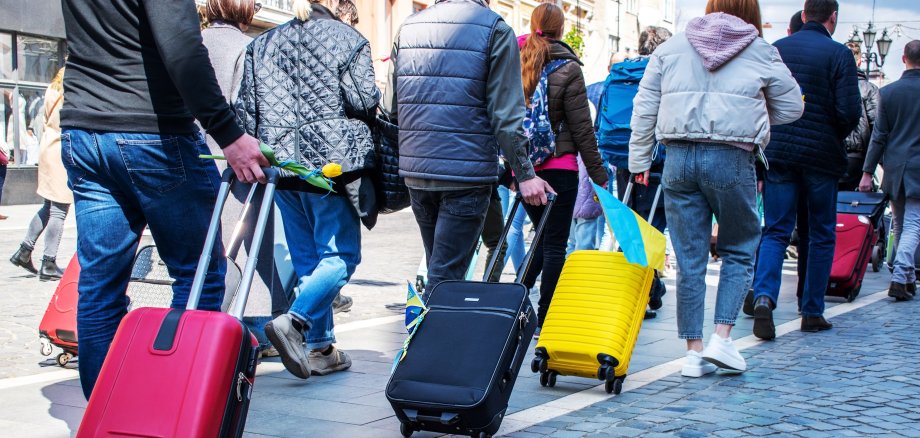 Ukrainische Flüchtlinge verlassen die Ukraine. Menschen mit Rollkoffern gehen hintereinander her.