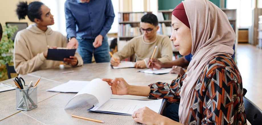 Eine muslimische Immigrantin sitzt am Tisch und sieht sich während des Unterrichts Blätter mit Grammatikaufgaben an.