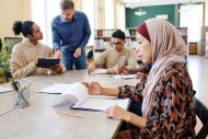 Eine muslimische Immigrantin sitzt am Tisch und sieht sich während des Unterrichts Blätter mit Grammatikaufgaben an.