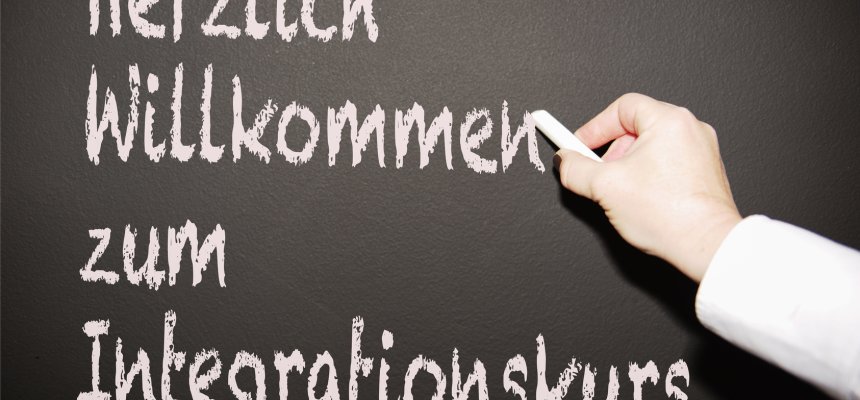 Lehrerin scheibt an die Tafel "Herzlich willkommen zum Integrationskurs"
