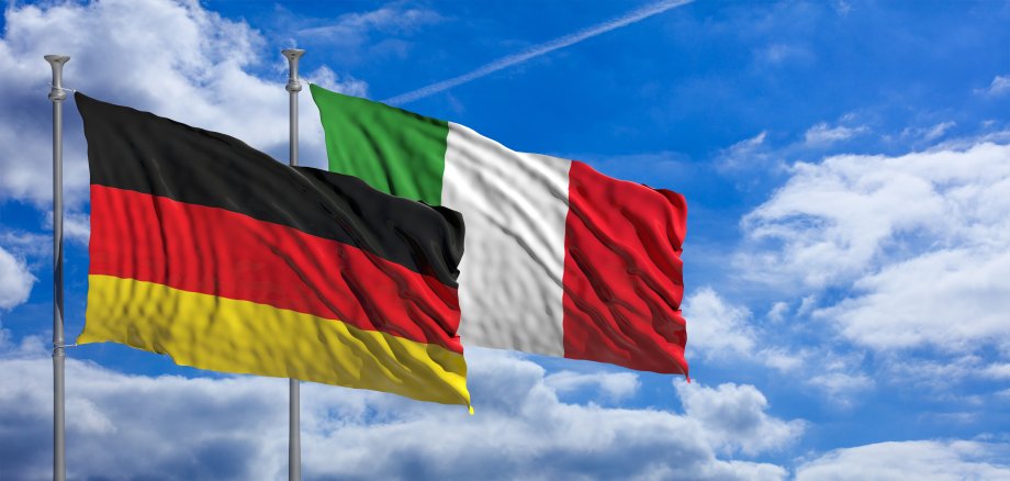 Italienische und deutsche Nationalflagge vor Sonne-Wolken-Hintergrund
