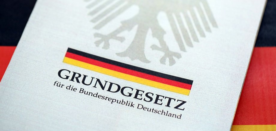 Deutsches Grundgesetz Das deutsche Grundgesetzbuch liegt vor dem Hintergrund der deutschen Flagge (Nahaufnahme).