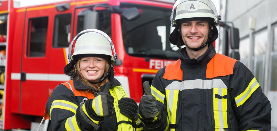 Feuerwehrmann und Feuerwehrfrau strecken den Daumen in die Kamera