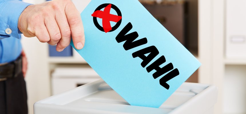 Hand hält Stimmzettel zur Wahl mit Wahlurne