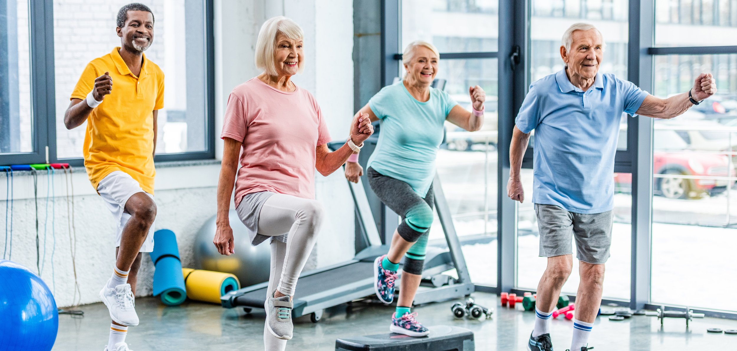 smiling multiethnic senior athletes synchronous exercising on step platforms at gym smiling multiethnic senior athletes synchronous exercising on step platforms at gym