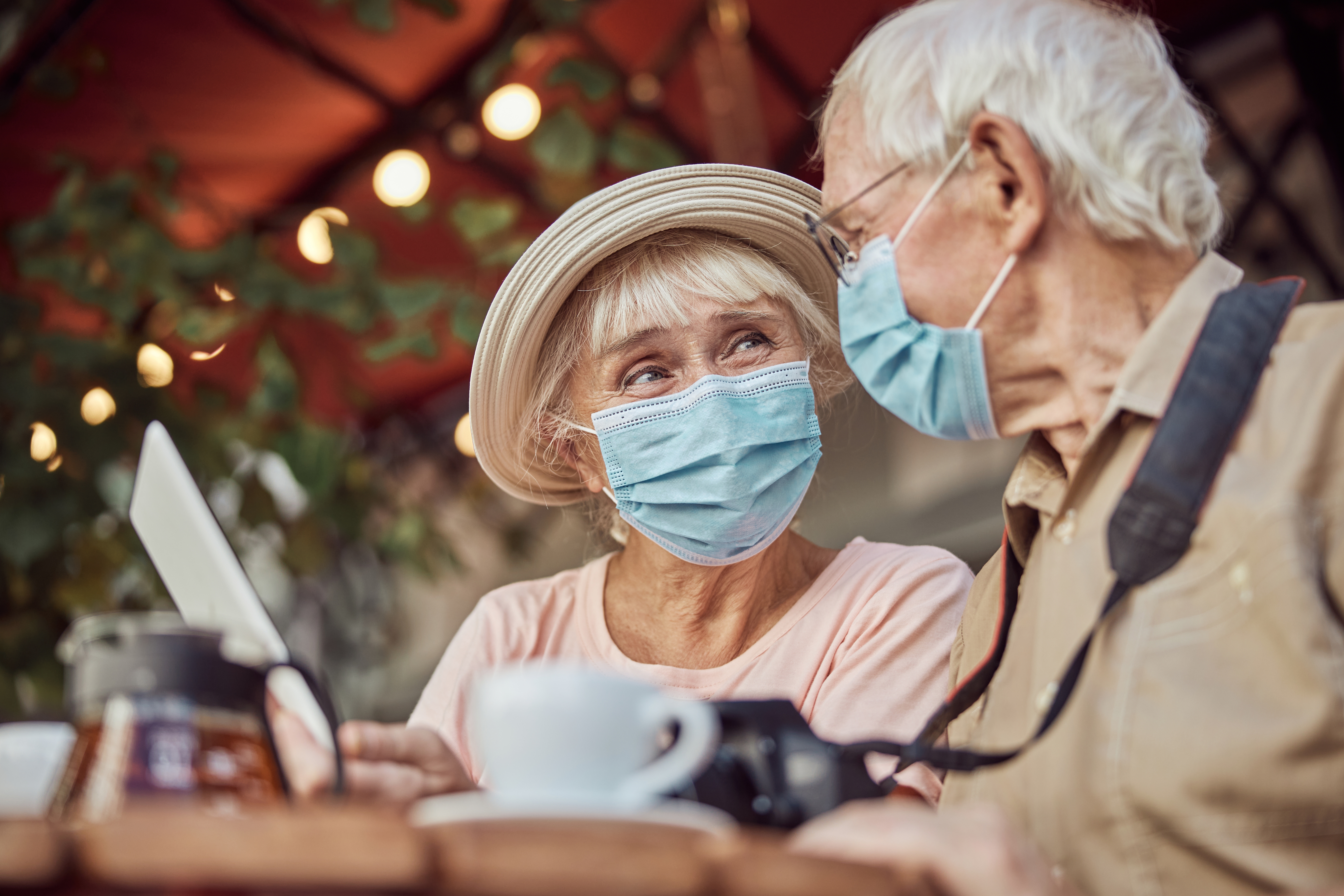 Zwei ältere Menschen sitzen in einem Straßencafé. Beide tragen eine medizinische Maske.