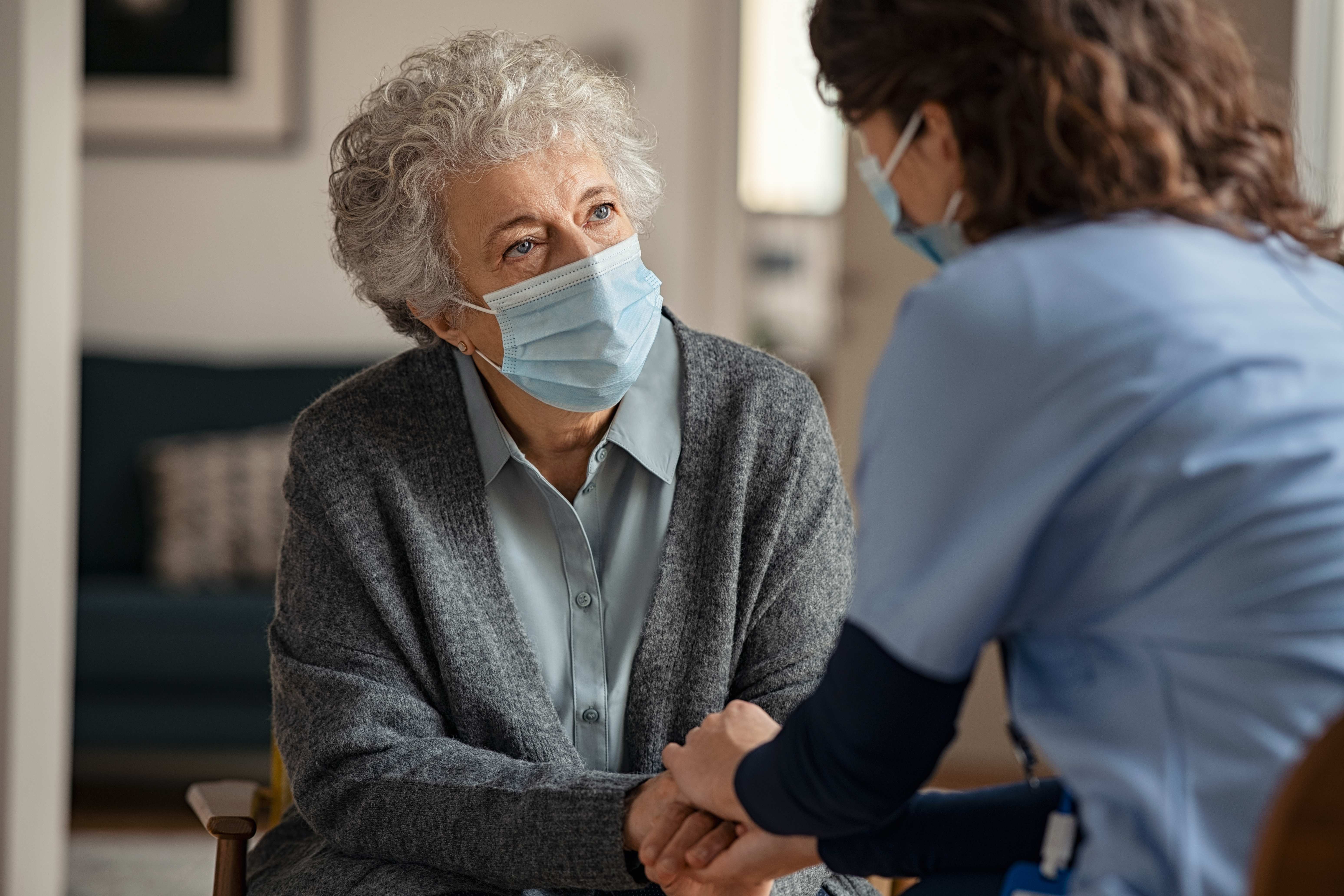 Ärztin, die mit einer älteren Patientin spricht. Beide tragen medizinische Masken.