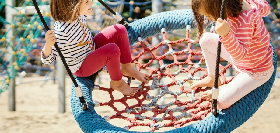 two little girls are swinging on a swing at the playground on a summer day Zwei Mädchen auf Spielplatz