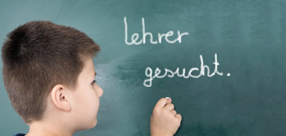 Junge schreibt "Lehrer gesucht" an eine Tafel