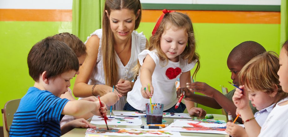 Kinder malen mit Erzieher im Kindergarten Viele Kinder malen mit Farbe zusammen mit Erzieher im Kindergarten