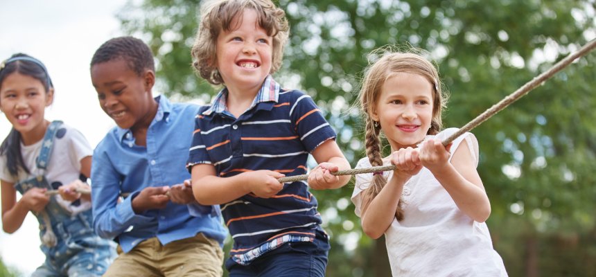 Glückliche Gruppe Kinder beim Tauziehen als Team in der Natur