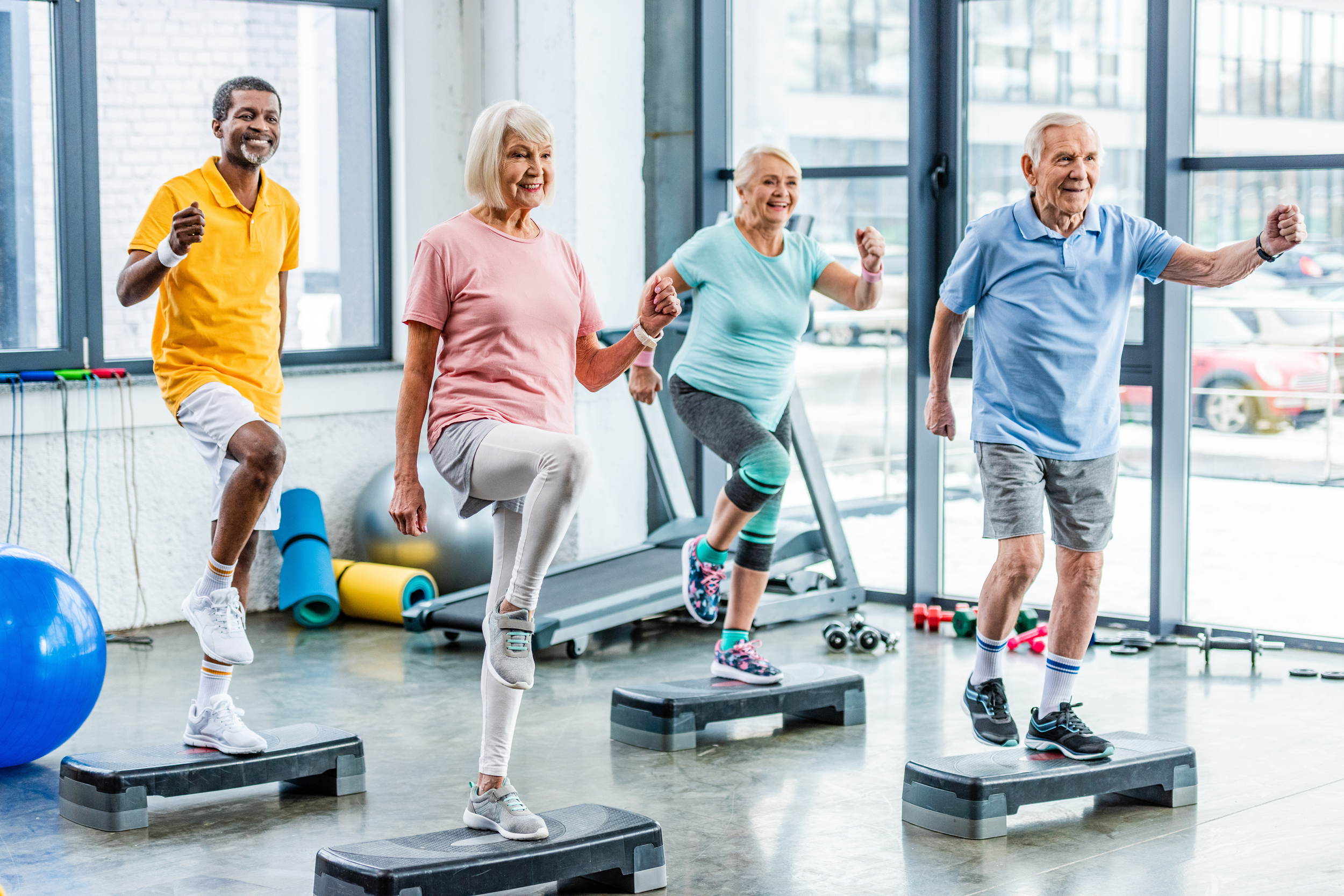 smiling multiethnic senior athletes synchronous exercising on step platforms at gym smiling multiethnic senior athletes synchronous exercising on step platforms at gym
