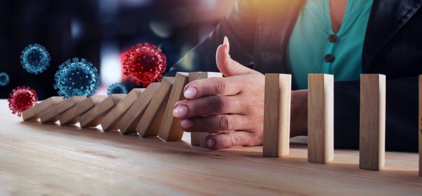 Businessfrau stoppt eine fallende Dominosteinreihe, über der Viren schweben. Ein Symbolbild für das Verhindern einer schweren Wirtschaftskrise durch Vireninfektionen. 