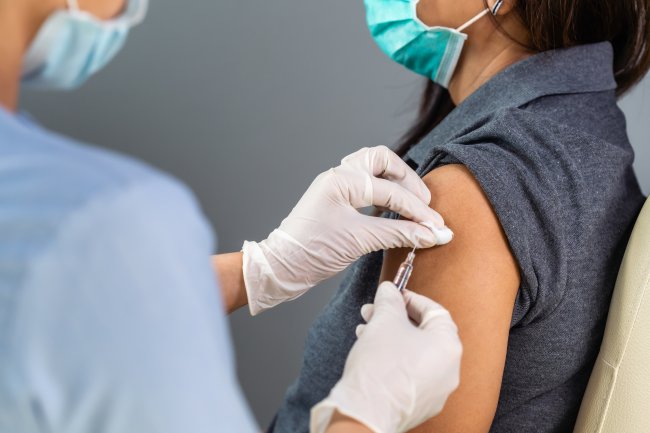 Arzt, der eine Spritze hält und einen Tupfer verwndet, bevor einem Patienten, der eine Maske trägt eine Injizierung gibt. Corona Virus Impfung.