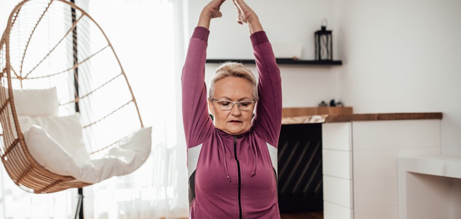 Sportliche Seniorin auf einer Yogamatte beim Training in ihrem Apartment. 