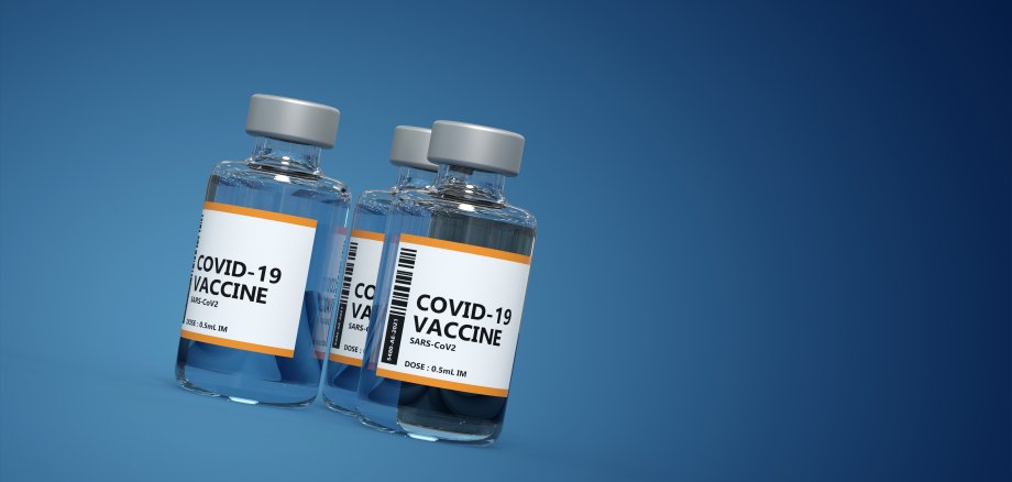 drei Fläschchen mit Covid-19 Impfstoff vor blauem Hintergrund
