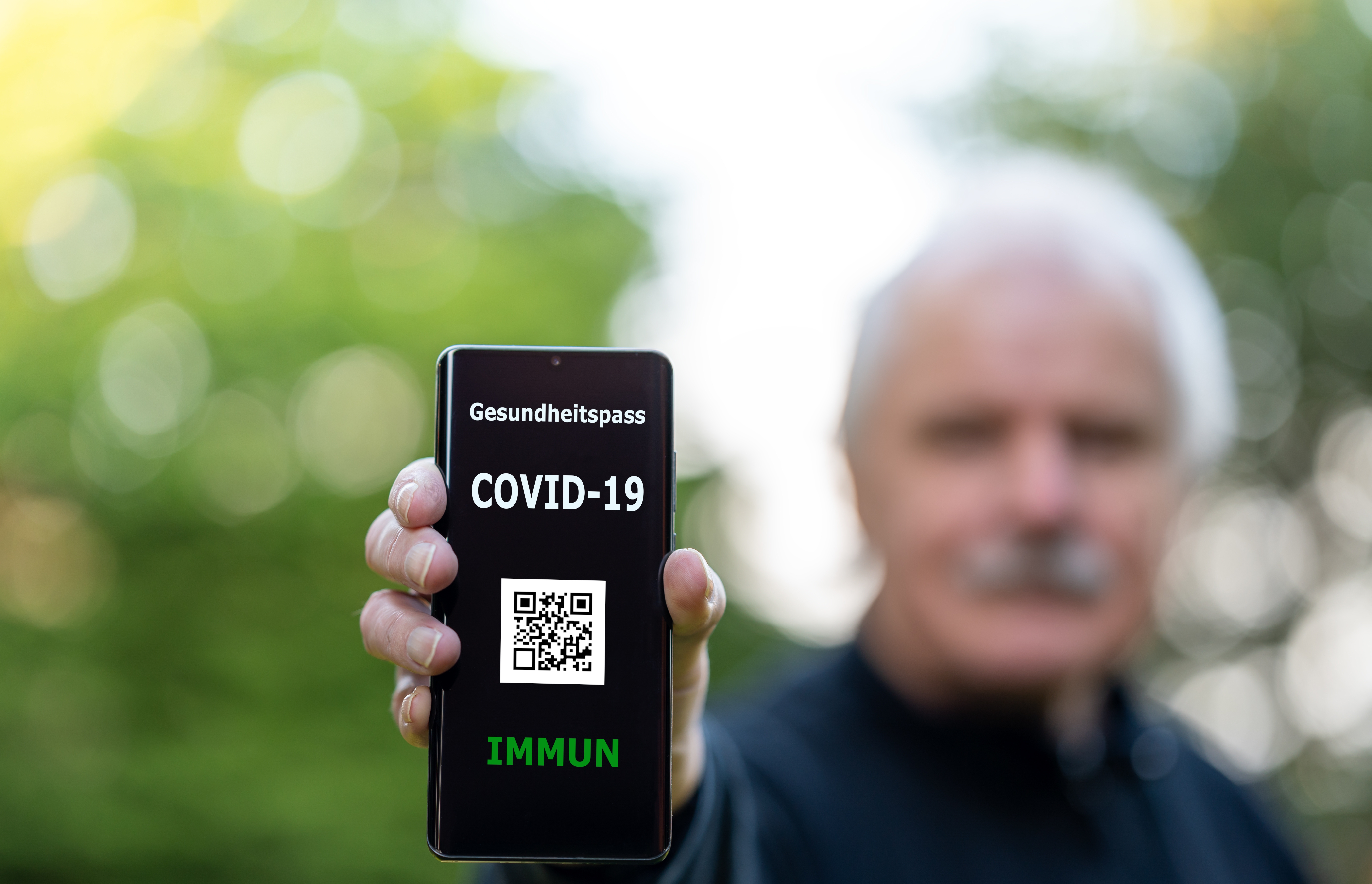 Älterer Herr zeigt digitalen Impfpass auf dem Smartphone, auf dem eine COVID-19 Impfung nachgewiesen wird.