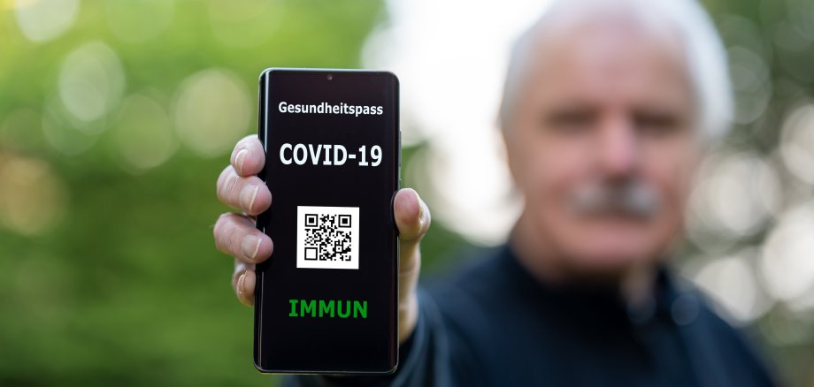 Älterer Herr zeigt digitalen Impfpass auf dem Smartphone, auf dem eine COVID-19 Impfung nachgewiesen wird.