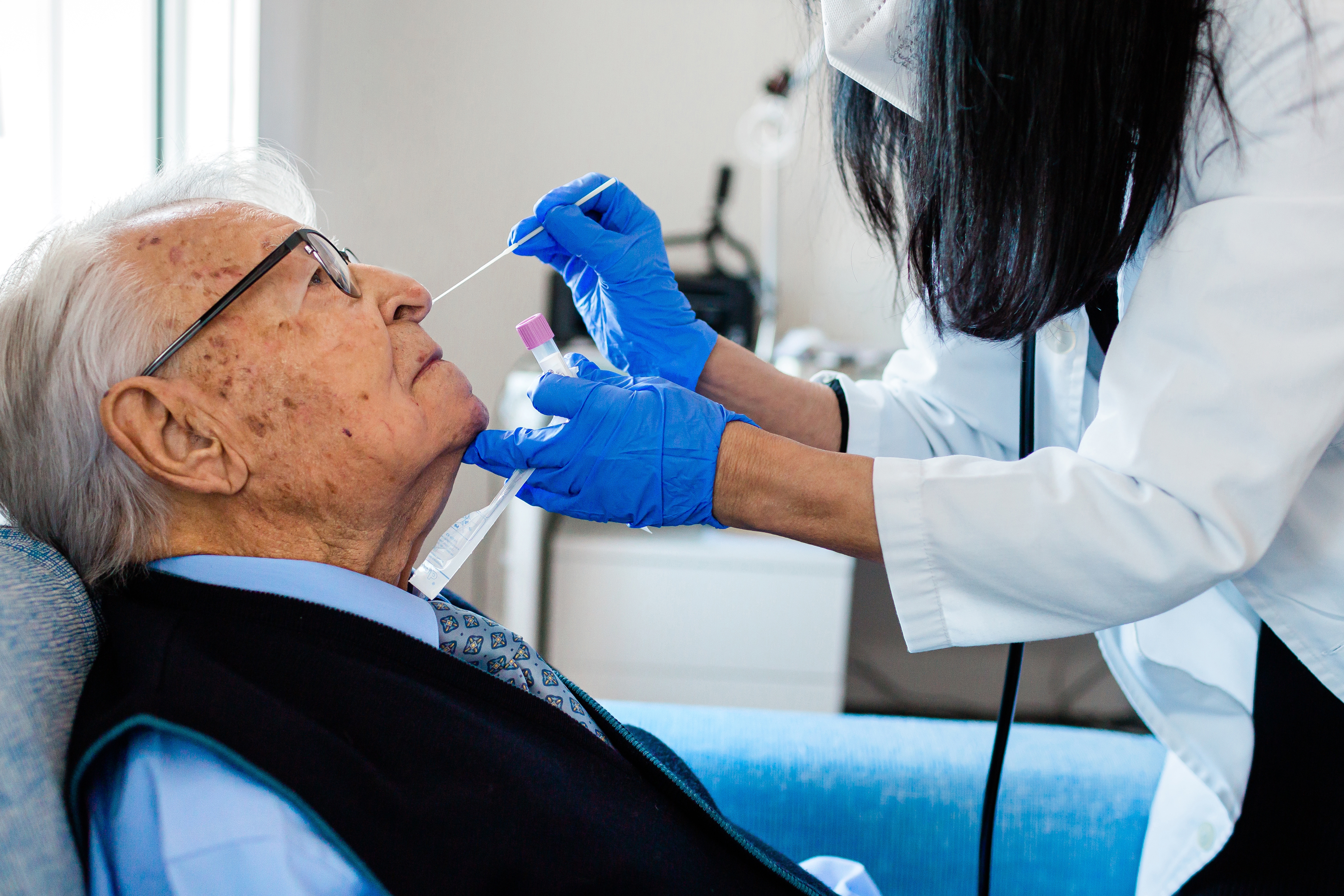 Krankenschwester, die einen Coronavirus PCR Test an einem älteren Mann in seiner Wohnung durchführt. 
