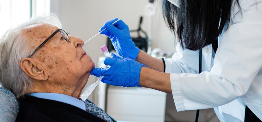 Krankenschwester, die einen Coronavirus PCR Test an einem älteren Mann in seiner Wohnung durchführt. 