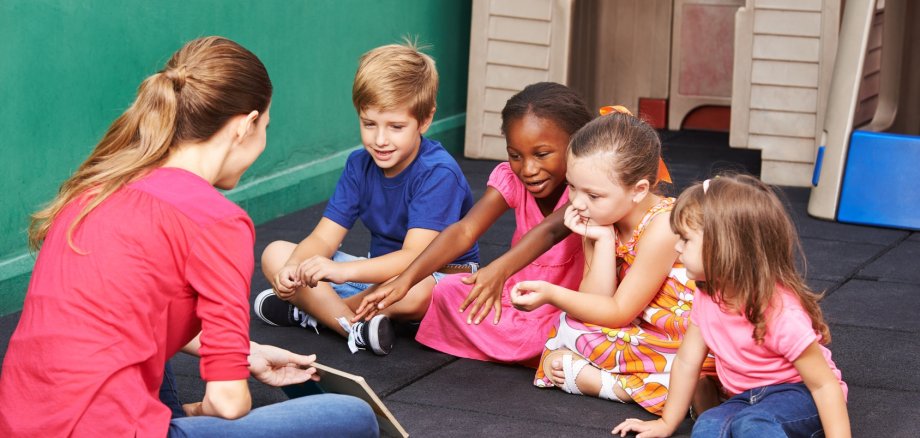 Gruppe Kinder redet über ein Buch im Kindergarten mit der Erzieherin