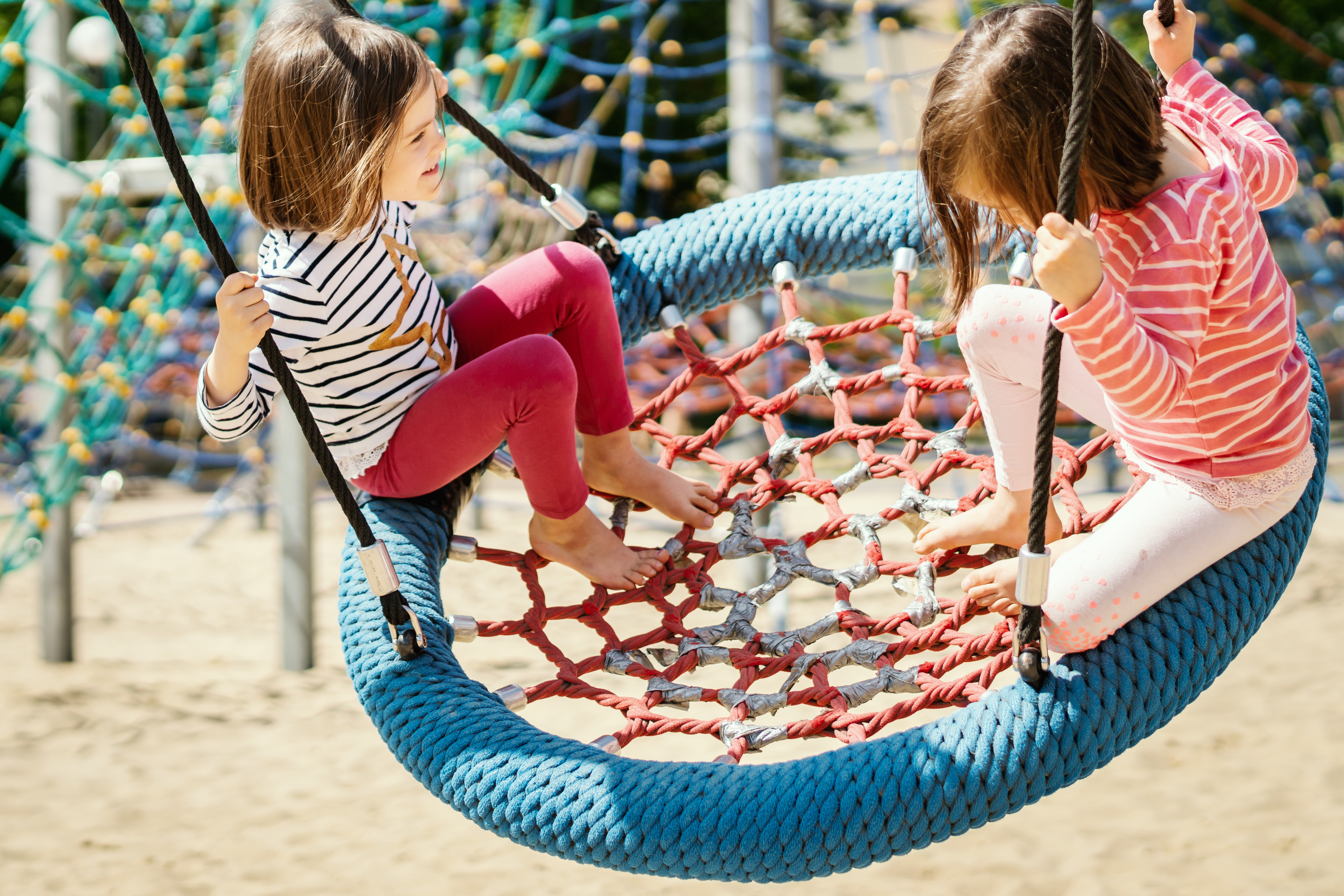 two little girls are swinging on a swing at the playground on a summer day Zwei Mädchen auf Spielplatz