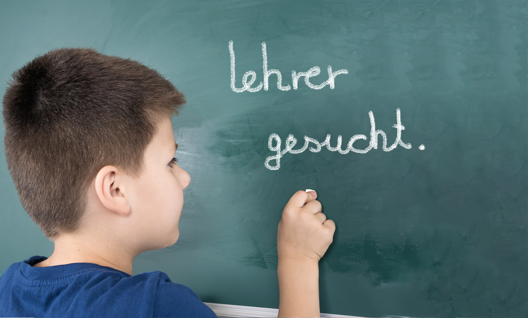 Junge schreibt "Lehrer gesucht" an eine Tafel