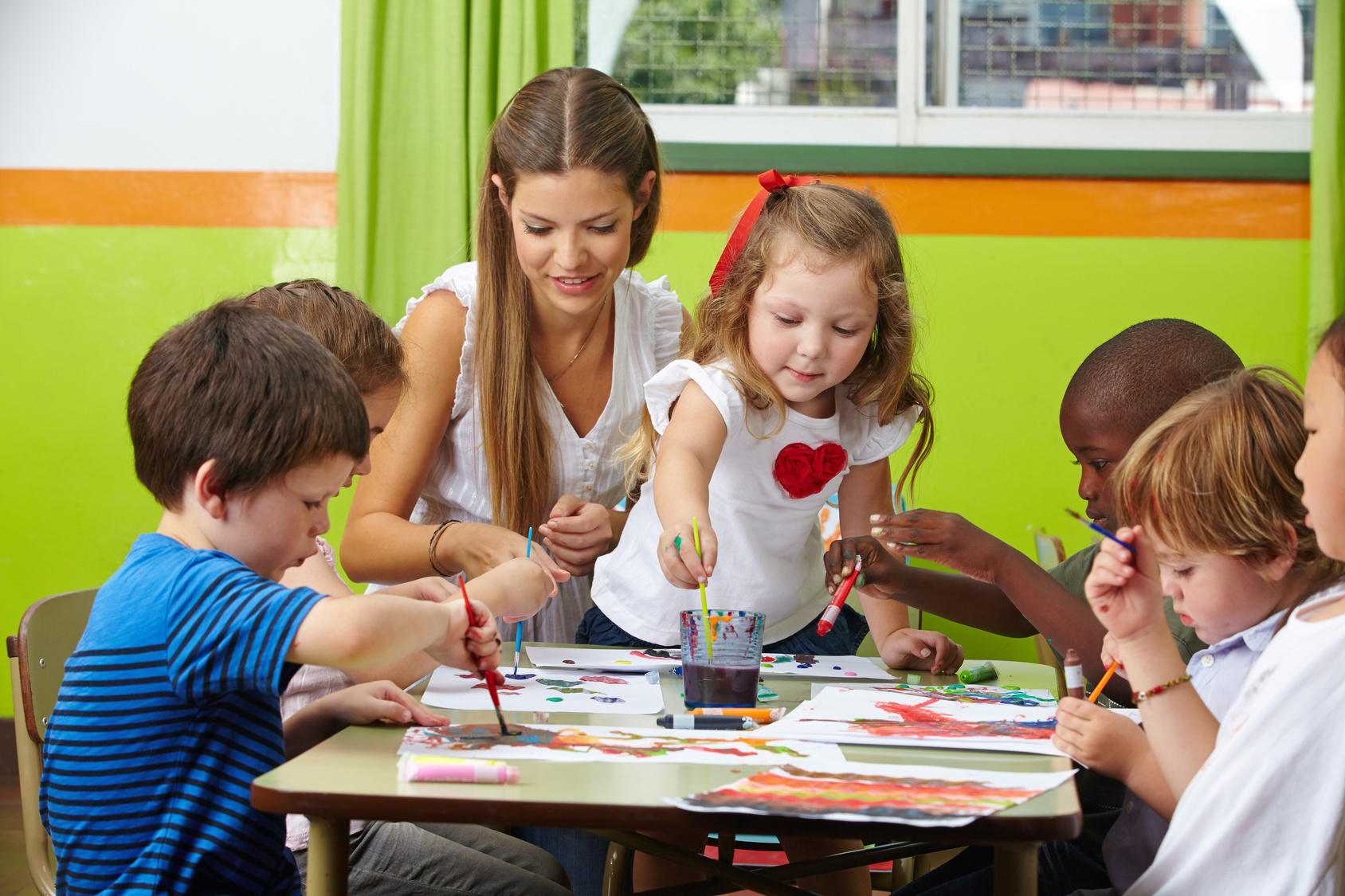 Kinder malen mit Erzieher im Kindergarten Viele Kinder malen mit Farbe zusammen mit Erzieher im Kindergarten