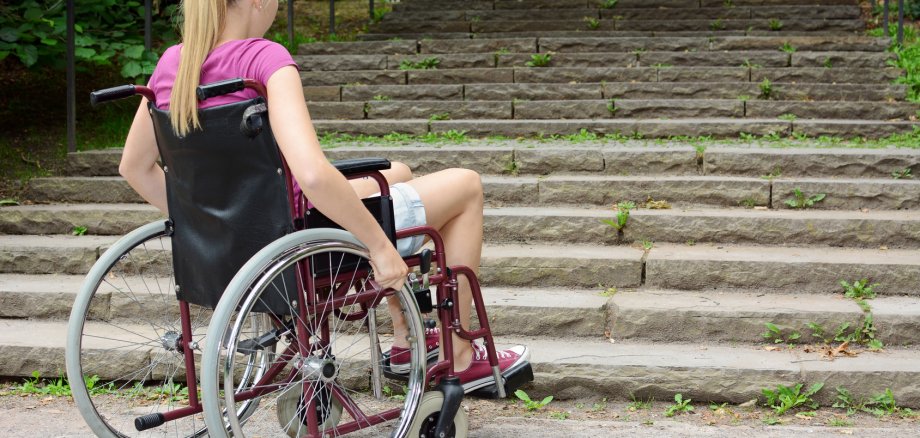Frau im Rollstuhl vor Treppe als Hindernis