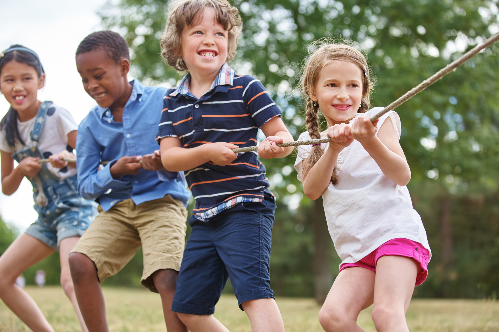Gruppe Kinder beim Tauziehen Glückliche Gruppe Kinder beim Tauziehen als Team in der Natur