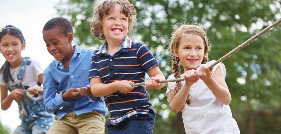 Glückliche Gruppe Kinder beim Tauziehen als Team in der Natur