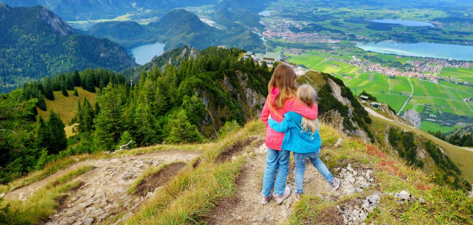 Zwei Schwestern genießen die malerische Aussicht vom Tegelberg, einem Teil der Ammergauer Alpen, in der Nähe der Stadt Füssen in Bayern, Deutschland.