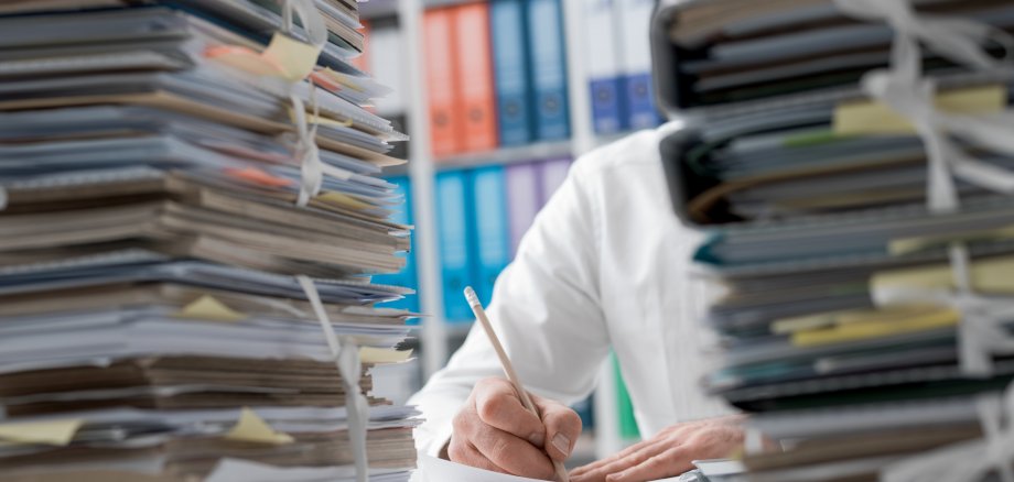 Ein Manager sitzt im Büro und hat Berge von Papierkram vor sich; er ist völlig überlastet. 