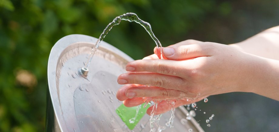 Hände fangen kühles Trinkwasser während der sengenden Sommerhitze auf.