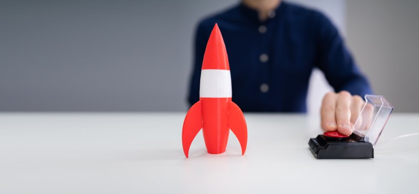 Mann drückt auf roten Knopf und rote Spielzeug Rakete steht vor ihm, die mit Kabel verbunden ist. 