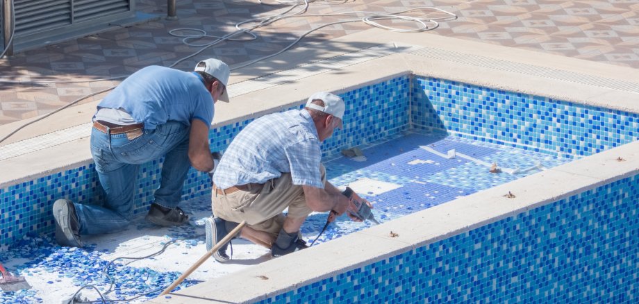Zwei Männer, die an einem Boden eines Schwimmbeckens arbeiten. 