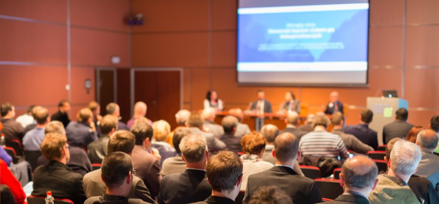 Publikum auf Konferenz mit Präsentation im Hintergrund